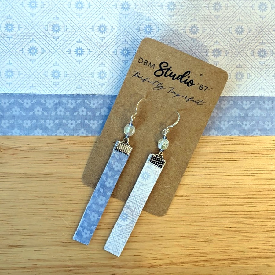 Thin rectangle dangle scrapbook paper earrings with silver metal accents and blue sparkly beads. Light blue floral and linear front and darker blue floral back. Back and front are shown.